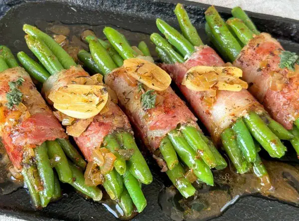 Grüne Bohnen im Speckmantel, mit Knoblauch und Kräutern, serviert in einer dunklen Pfanne.